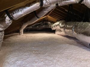 attic with large foil-wrapped hvac ducts running along the ceiling and pink insulation on the floor.