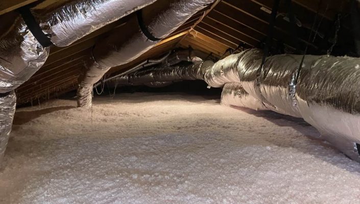 Attic with large foil-wrapped HVAC ducts running along the ceiling and pink insulation on the floor.