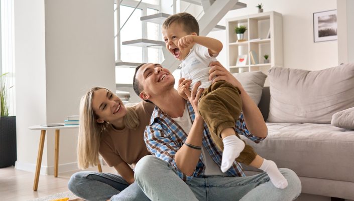 happy young family couple having fun playing with cute, smiling toddler in home.