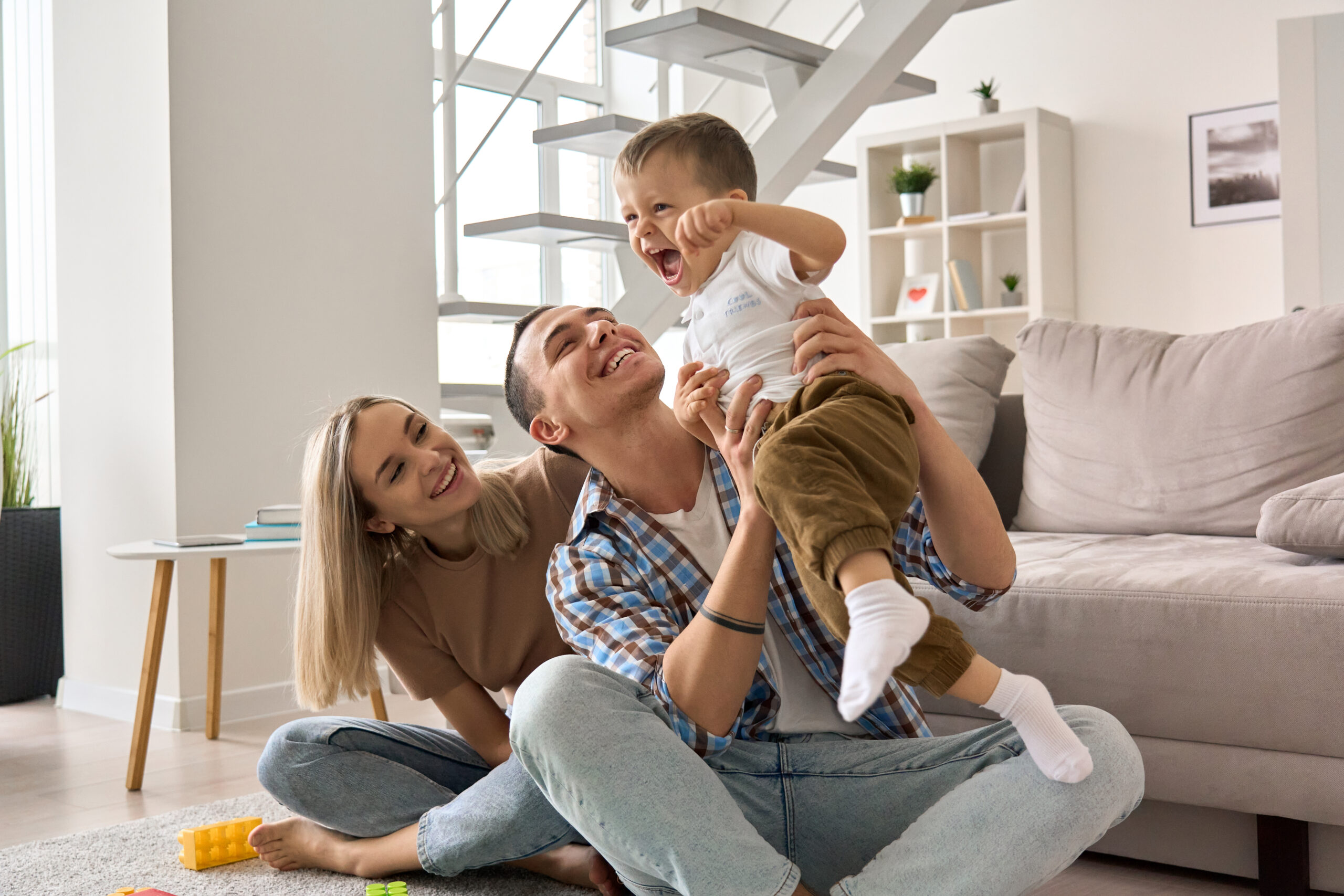 happy young family couple having fun playing with cute, smiling toddler in home.